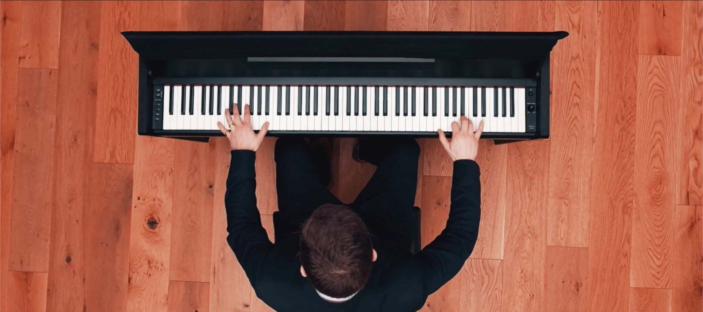 Overhead view of Finn playing a black upright piano on a wooden floor